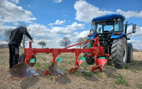 Rolnik przygotowuje pług do orania ziemi. Błękitne niebo z chmurami nad polem.