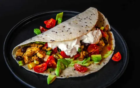 Ein köstliches Fajitas-Rezept: Tortilla gefüllt mit Hähnchen, Gemüse, Avocado und Sour Cream, garniert mit Tomaten.