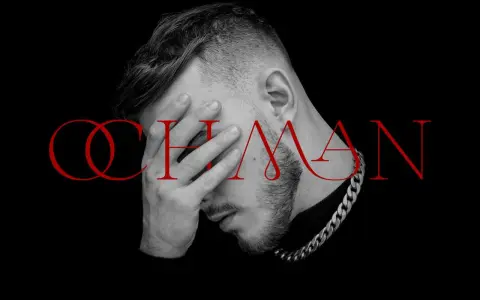 Krystian Ochman - nowa płyta. Artysta z dłonią na twarzy, w tle czerwony napis "OCHMAN".