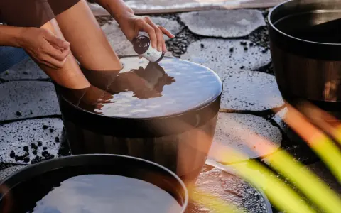 A person adds a few drops from a small bottle to a wooden tub filled with water, creating the best natural foot soak.