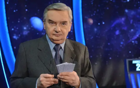 Starsza osoba w garniturze trzyma karty z napisem "1 z 10", gotowa do emisji.