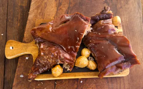 Delicioso cochinillo al horno, crujiente y jugoso, servido con patatas asadas sobre tabla de madera.