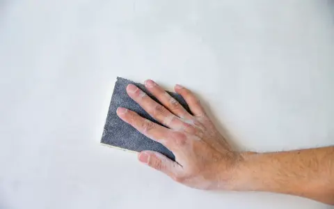 Mano che leviga una parete con carta vetrata, mostrando le sue caratteristiche abrasive per una finitura liscia.