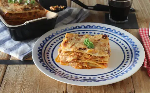 Una porción de lasaña de atún, dorada y gratinada, servida en un plato con diseño azul.