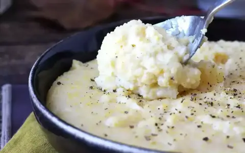 Kremowa polenta, idealna do prostego polenta przepis, posypana świeżo mielonym pieprzem, nabierana łyżką z czarnej miski.