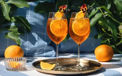 Dwa kieliszki Aperol Spritz z plastrami pomarańczy i kwiatami. Czy aperol można pić sam? Tak, ale najlepiej smakuje w towarzystwie!