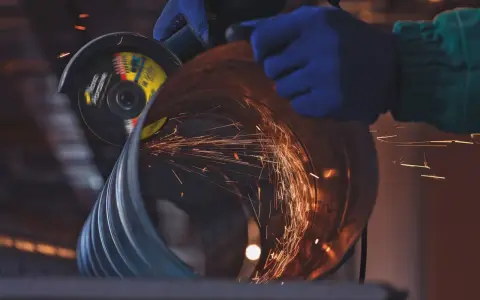Manos enguantadas usan una radial para cortar un tubo, generando chispas. Un accidente con radial es un riesgo constante.