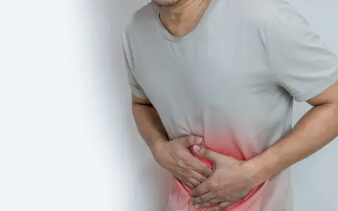 Mężczyzna trzyma się za brzuch, odczuwając ból w okolicy jelita grubego. Czerwony obszar podkreśla miejsce dolegliwości.