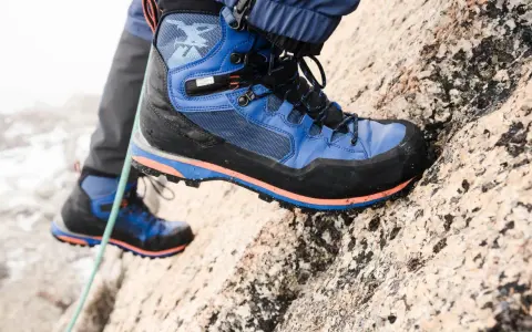 Close-up of a blue and black hiking boot with orange accents, gripping a rocky surface.