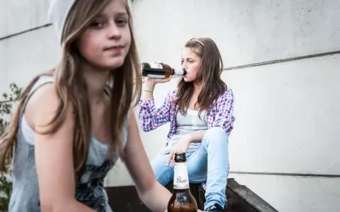 Dwie nastolatki piją piwo, co może być początkiem alkoholizmu wśród młodzieży.