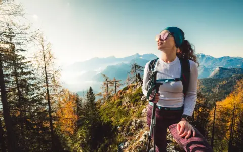 Kobieta w sportowym outfit w górach, z kijkami trekkingowymi, podziwia jesienny krajobraz.