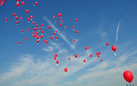 Många röda heliumballonger stiger mot en klarblå himmel med tunna moln.