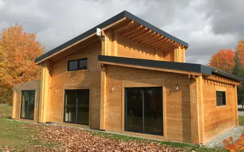 Une belle maison en bois, prête à accueillir ses habitants. L'automne arrive, les feuilles tombent autour de cette construction chaleureuse.