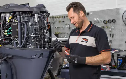 Un mécanicien effectue l'entretien d'un moteur hors-bord 4 temps Yamaha, tenant une bougie et un outil.