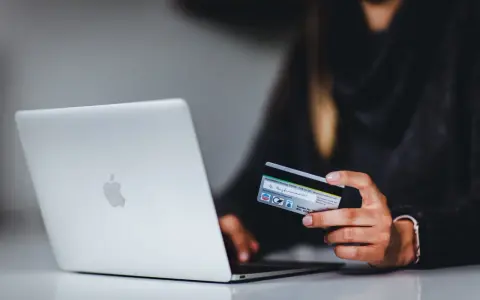 Kobieta z kartą kredytową przy laptopie. Dowiedz się, jak bezpiecznie korzystać z komputera podczas zakupów online.
