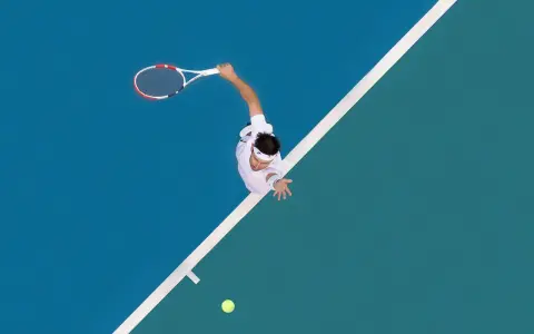 A tennis player in mid-serve, racket raised, on a blue and green court. The white lines of the court are like brad walls, guiding the game.