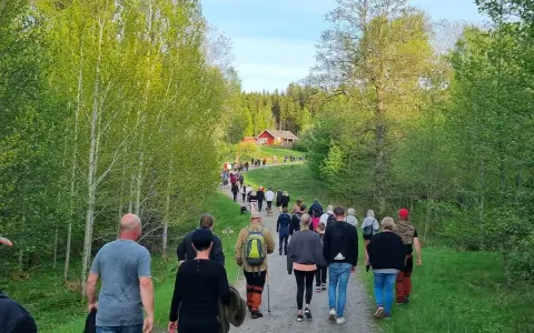 En grupp människor på en nattvandring Kinnekulle, på en grusväg genom en lummig skog. En röd stuga syns i bakgrunden.