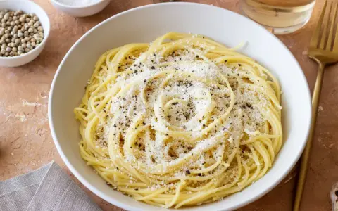 Miseczka spaghetti posypana parmezanem i pieprzem, obok przyprawy i czosnek.
