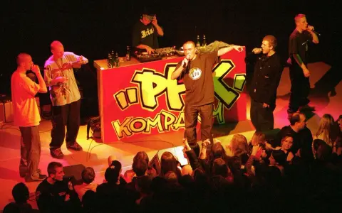 Raperzy na scenie przed czerwonym banerem z napisem "PFK Kompakt", publiczność w pierwszym rzędzie.
