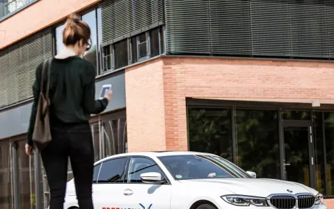 Frau mit Smartphone wartet auf FREE NOW Fahrt. Keine Beschwerde, nur Vorfreude auf die Fahrt.