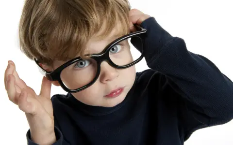 Chłopiec z niebieskimi oczami poprawia okulary, zastanawiając się nad nadwzrocznością u dzieci kiedy okulary są potrzebne.