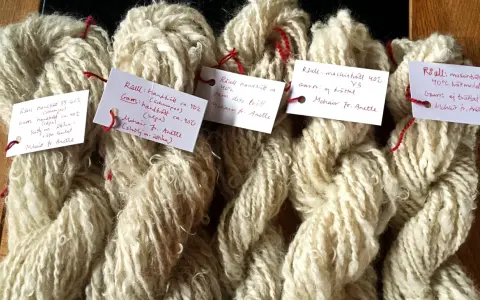 Buntar av ljusbeige garn, troligen mohair ull, med handskrivna etiketter som beskriver tvättmetoder och ursprung.