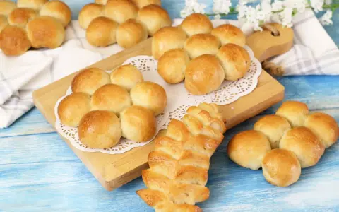 Morbidi panini al latte dorati, alcuni disposti a grappolo su un tagliere, altri su un panno bianco.
