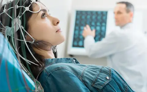 Frau mit EEG-Kappe für eeg medizinische Untersuchung, Arzt deutet auf Bildschirm mit Gehirnscans.