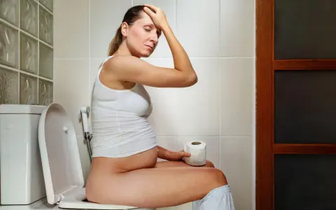 Donna incinta sul water, con la mano sulla fronte, preoccupata per la cacca in gravidanza.