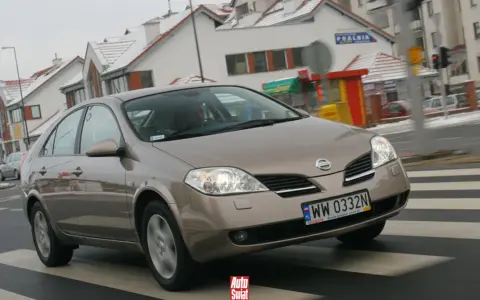 Brązowy Nissan Primera przejeżdża przez pasy na tle zaśnieżonych domów.