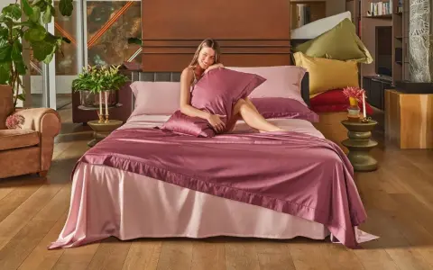 Una donna sorride su un letto con lenzuola rosa. Per mantenerle fresche, si lavano a 40 gradi.