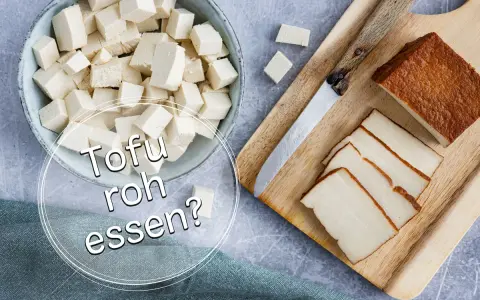 Würfel und Scheiben von Tofu liegen neben einem Messer auf einem Holzbrett. Die Frage "Kann man Tofu roh essen?" wird gestellt.