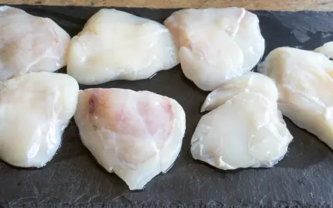 Plusieurs morceaux de lotte crue, prêts pour une cuisson au four, sont disposés sur une planche d'ardoise.