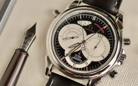 Elegante cronografo rattrapante Omega De Ville con quadrante nero e contatori argentati, accanto a una penna stilografica.