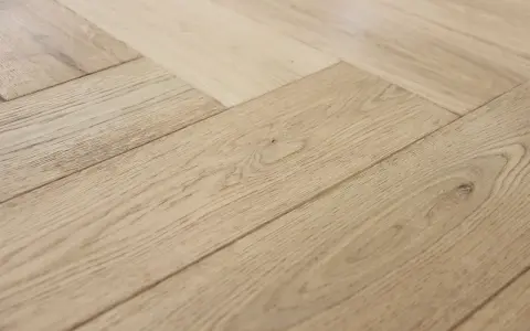 Jasne, drewniane deski ułożone we wzór jodełki francuskiej tworzą elegancką podłogę.