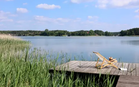 Spokojne kaszubskie jeziora, drewniany pomost z leżakiem i książką, otoczone trzcinami i lasem.