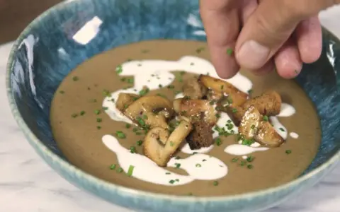 Crema de champiñones servida en un cuenco azul, decorada con champiñones salteados, picatostes y un chorrito de nata.