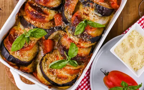 Gebackene Auberginen-Tomaten-Schichten in Auflaufform, garniert mit Basilikum. Perfekt, um Auberginen haltbar zu machen und köstlich zu genießen.