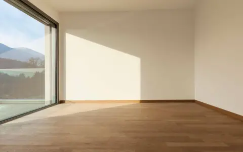 Habitación vacía con suelo de madera y gran ventanal de cristal planitherm que ofrece vistas a montañas.