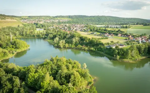 Grüne Hügel, ein Dorf und der glitzernde Klostersee Triefenstein unter blauem Himmel.