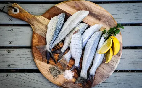 Plusieurs poissons frais sur une planche à découper en bois avec du sel, du poivre et des quartiers de citron.
