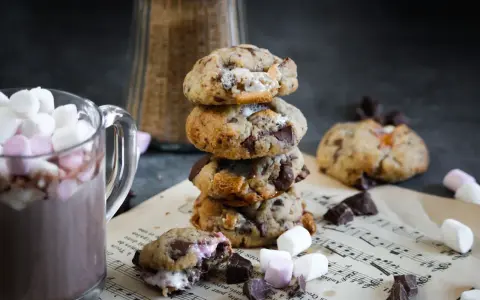Un cookie chamallow fondant, empilé avec d'autres, à côté d'une tasse de chocolat chaud garnie de guimauves.