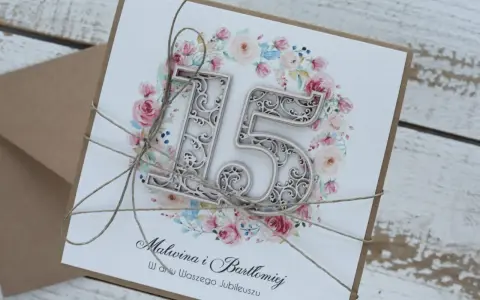 Elegancka kartka z napisem "15 rocznica ślubu" i imionami Malwina i Bartłomiej, ozdobiona kwiatowym wiankiem i sznurkiem.