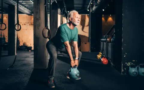 Älterer Mann macht Stabi-Training mit Kettlebell im Fitnessstudio.