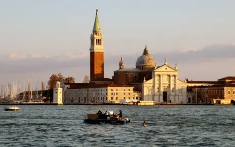 Le campanile et l'église de San Giorgio Maggiore à Venise se reflètent sur l'eau. Un bateau transporte des passagers.