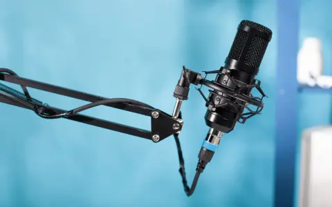 Czarny mikrofon pojemnościowy na wysięgniku, gotowy do nagrania podcastu. W tle niebieskie tło.