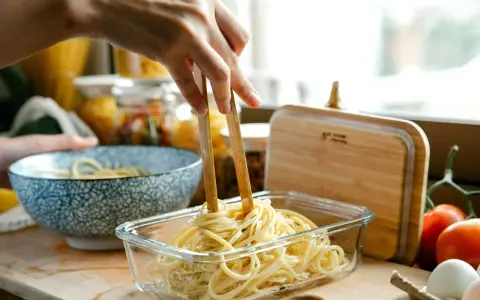 Dłoń trzymająca pałeczki wyciąga makaron spaghetti z szklanego pojemnika.