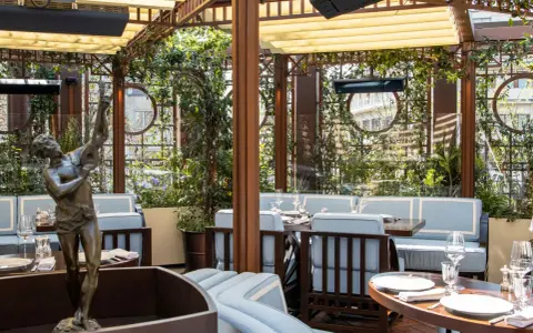 Terrazza lussuosa con statue e piante, tavoli apparecchiati per un'esperienza culinaria al **Wilde Milano**.