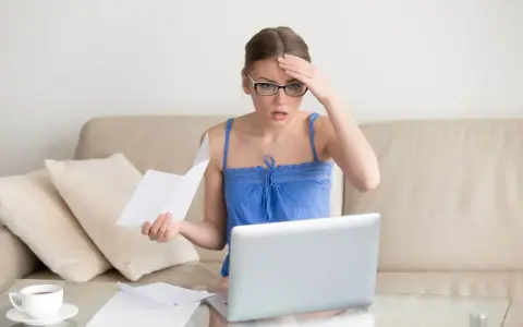 Zmartwiona kobieta z okularami sprawdza dokumenty na laptopie, martwiąc się o przedawnienie długu za czynsz mieszkaniowy.