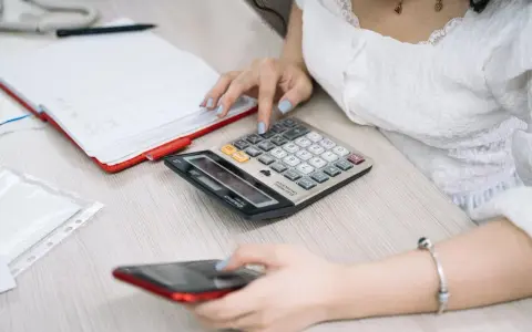 Kobieta liczy na kalkulatorze, przygotowując się do rozliczenia podatkowego w Holandii. Obok leży telefon i notatnik.